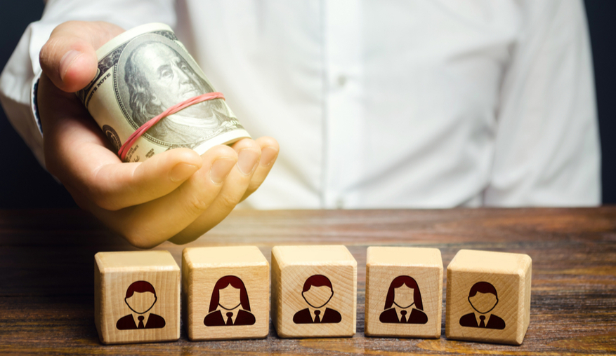 A man holds out money dollars over blocks with employees.