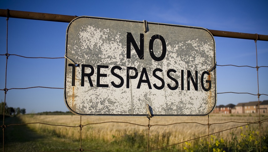 no trespassing sign against backdrop of farmland