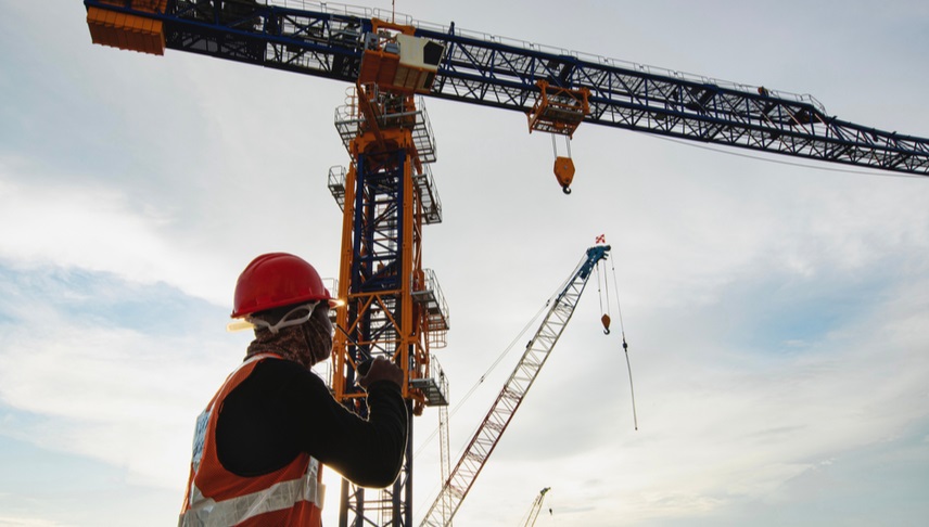 rigger talking to a crane operator in a walkie talkie while checking the movement of the crane