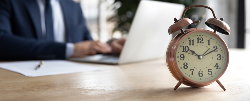 clock on a desk with an attorney doing his work in a laptop as a background