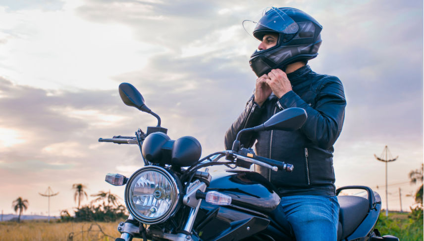 man sitting on a motorcycle fastening his helmet