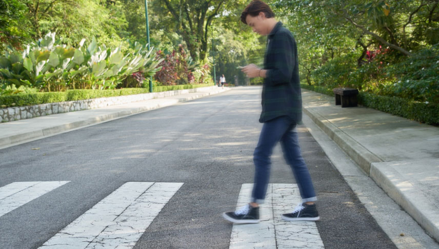 man crossing pedestrian and looking at his cellphone